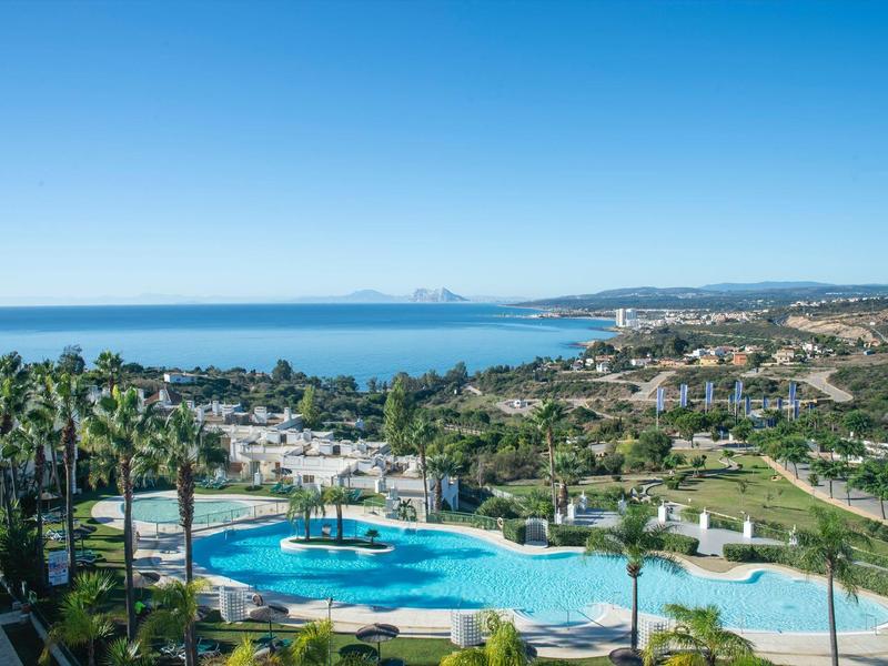 Blaue Lagunenpools mit Palmen vor Küstenlandschaft und Meer unter klarem blauen Himmel.