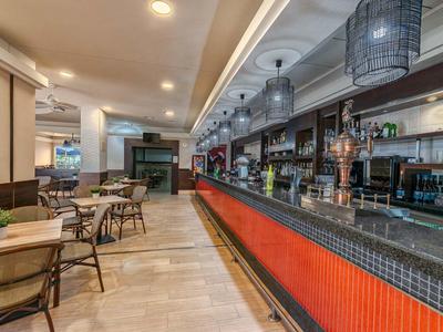 Moderner Gastraum mit langem Tresen, Holztischen und Stühlen, heller Beleuchtung und dekorativer Decke.