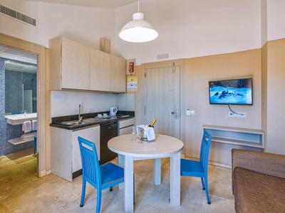 Kleine Küche mit runden Holztisch, zwei blauen Stühlen, Waschmaschine und Fernseher an der Wand.