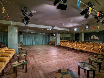 Großer Raum mit Holzboden, Sitzreihen an den Seiten und Bühnenlicht an der Decke.