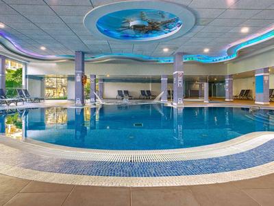 Innen-Schwimmbad mit blauem Wasser, runder Form, großen Fenstern und Deckenbeleuchtung.