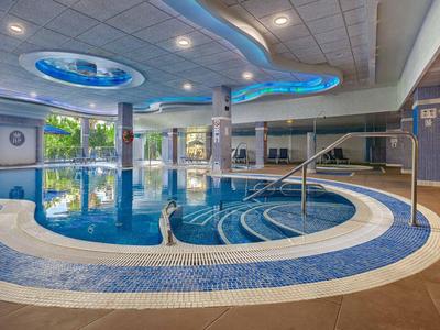 Innenbereich mit großem runden Schwimmbad, blauen Mosaikfliesen und runder Deckenbeleuchtung.