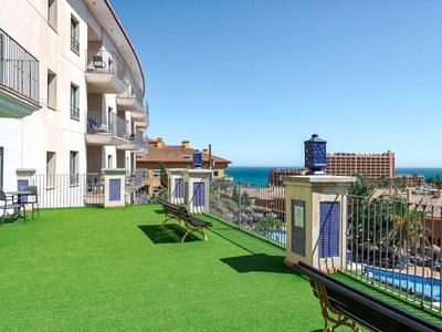 Blick auf Balkon mit grünem Kunstrasen, Bänken und Meer im Hintergrund unter klarem Himmel.
