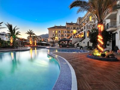 Area piscina serale di un hotel con palme e edifici illuminati.