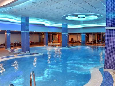 Großes Hallenbad mit blauer Beleuchtung, Säulen und runden Deckenelementen in modernem Design.