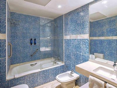 Badezimmer mit blauen Mosaikfliesen, Badewanne, Bidet, Waschbecken und großem Spiegel.
