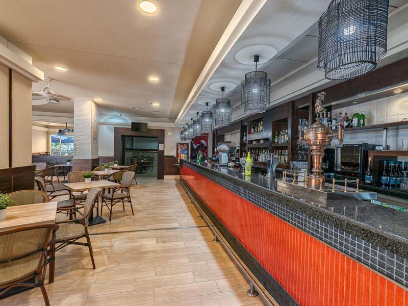 Moderner Gastraum mit langem Tresen, Holztischen und Stühlen, heller Beleuchtung und dekorativer Decke.