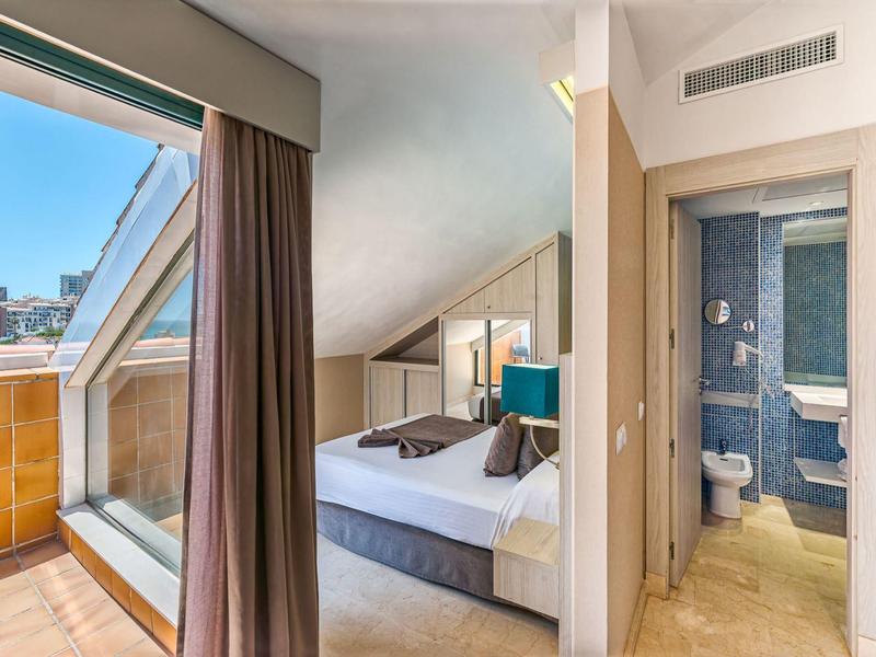 Helles Schlafzimmer mit Doppelbett, Zugang zum Balkon und angrenzendem Badezimmer.