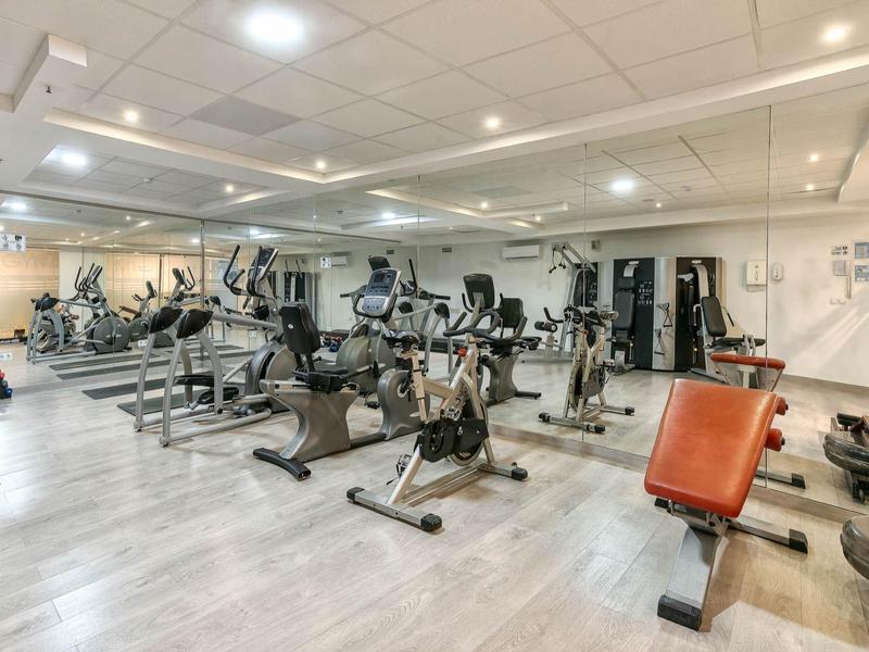 Moderner, heller Fitnessraum mit verschiedenen Trainingsgeräten und großen Spiegeln an der Wand.