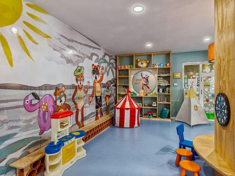 Bunter Spielraum mit Wandgemälde, Spielküche, Zelt, Regalen und bunten Kindermöbeln.