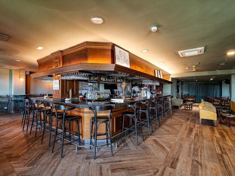 Elegante Bar mit Holzboden, hohen Stühlen und modernen Beleuchtungselementen in warmem Farbton.