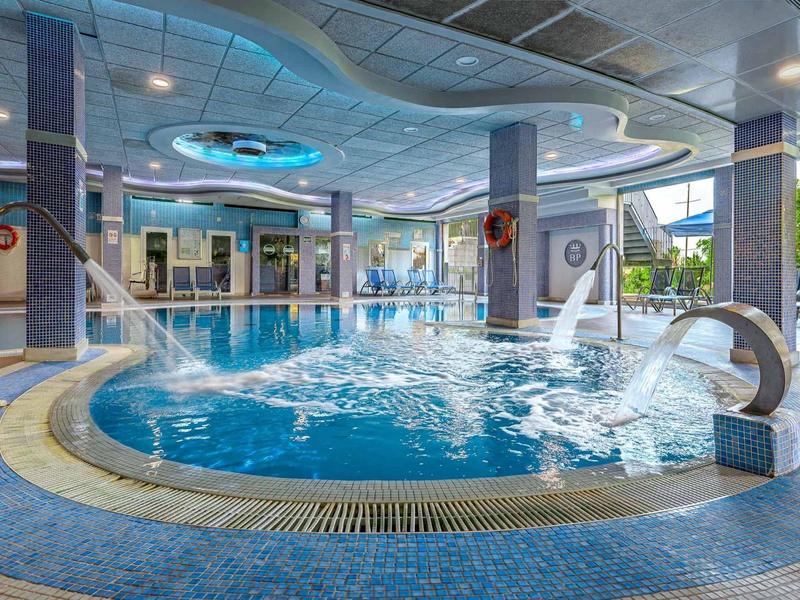 Moderner Innenpool mit Rundform, blauer Fliesen, Wasserspielen und großen Fenstern.