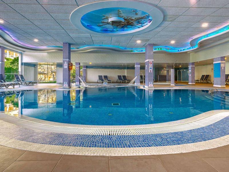 Innen-Schwimmbad mit blauem Wasser, runder Form, großen Fenstern und Deckenbeleuchtung.