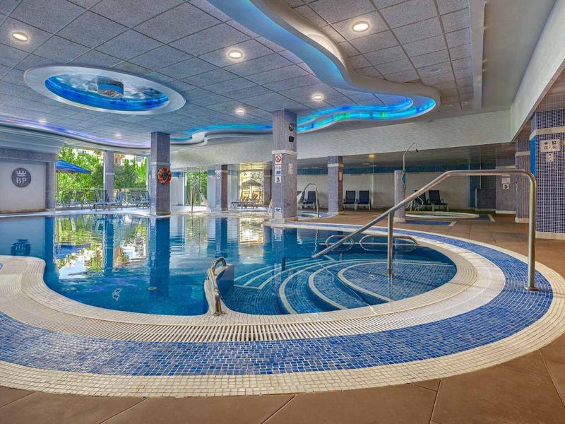 Innenbereich mit großem runden Schwimmbad, blauen Mosaikfliesen und runder Deckenbeleuchtung.