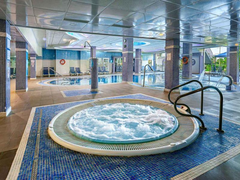 Innenbereich mit rundem Whirlpool, blauen Bodenfliesen und großen Fenstern zum Garten.