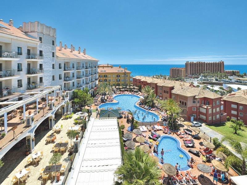 Große Hotelanlage mit Schwimmbädern, Sonnenterrassen, Palmen und Meer im Hintergrund bei klarem Himmel.