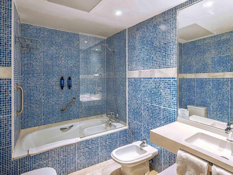 Badezimmer mit blauen Mosaikfliesen, Badewanne, Bidet, Waschbecken und großem Spiegel.