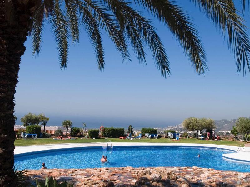 Kleiner Pool mit rundem Rand und Palmen, dahinter Grasfläche und weiter Blick aufs Meer.