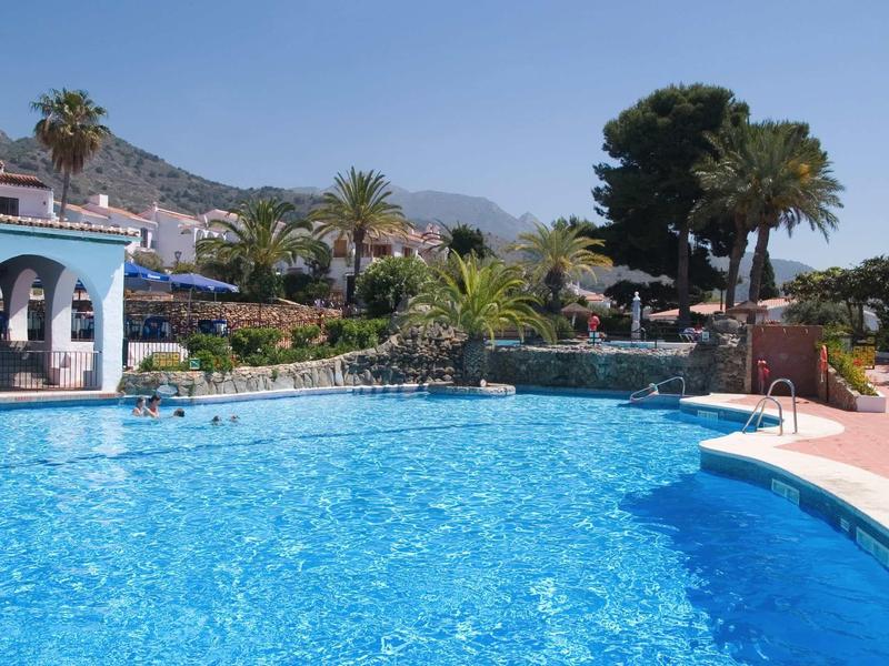 Großer blauer Schwimmbad mit Palmen, Bergen im Hintergrund und blauen Himmel an sonnigem Tag.