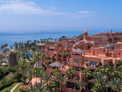 Blick auf ein Hotelresort mit roten Gebäuden, Palmen und Blick auf das Meer unter blauem Himmel