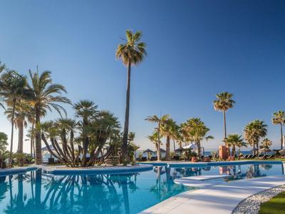 Großer Pool mit Palmen und blauem Himmel in einer Hotelanlage.