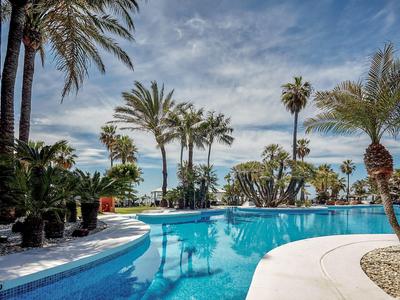 Pool mit kristallklarem Wasser, umgeben von Palmen und blauem Himmel im Ferienresort.