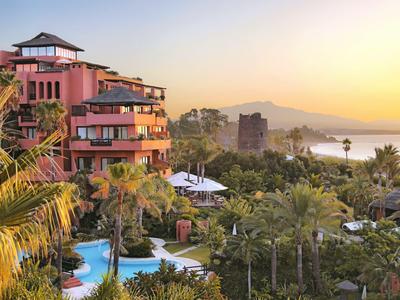 Hotelresort mit Pool, Palmen und Bergen bei Sonnenuntergang am Meer.