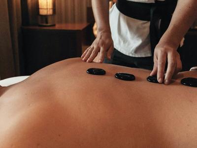 Person erhält Hot-Stone-Massage mit schwarzen Steinen auf dem Rücken.