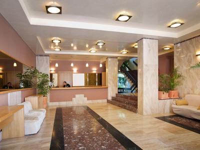 Jasny hol hotelowy z recepcją, sofami i marmurową podłogą.