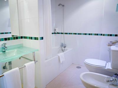 Helles Badezimmer mit Badewanne, Glaswaschbecken, Toilette, Bidet und weißen Handtüchern.