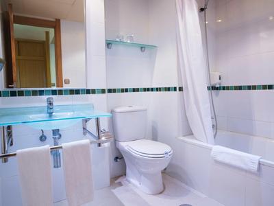 Kleines weißes Badezimmer mit Toilette, Glaswaschbecken und Badewanne mit Duschvorhang.