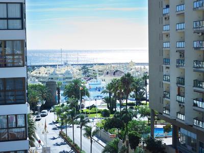 Blick auf Hafen mit Yachten und Palmen zwischen hohen Wohngebäuden bei klarem Himmel.