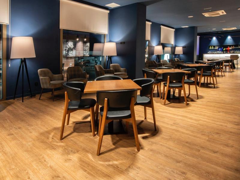 Modern eingerichteter Gastraum mit Holztischen, Stühlen und warmen Lampen auf Parkettboden.