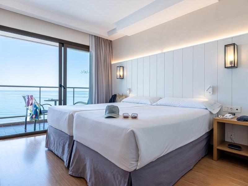 Helles Schlafzimmer mit großem Doppelbett, Nachttisch, Wandlampen und Balkon mit Meerblick.