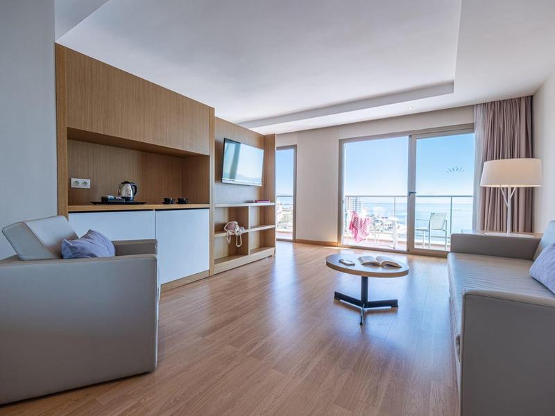 Helles Wohnzimmer mit Holzfußboden, grauen Sofas, großem Fenster und modernem TV-Bereich.