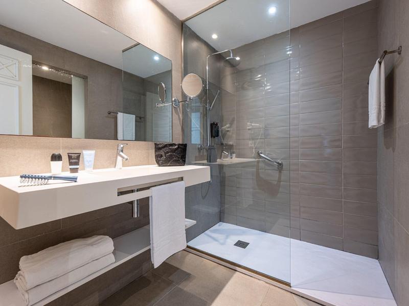 Modernes Badezimmer mit weißem Doppelwaschbecken, großen Spiegeln und ebenerdiger Dusche.