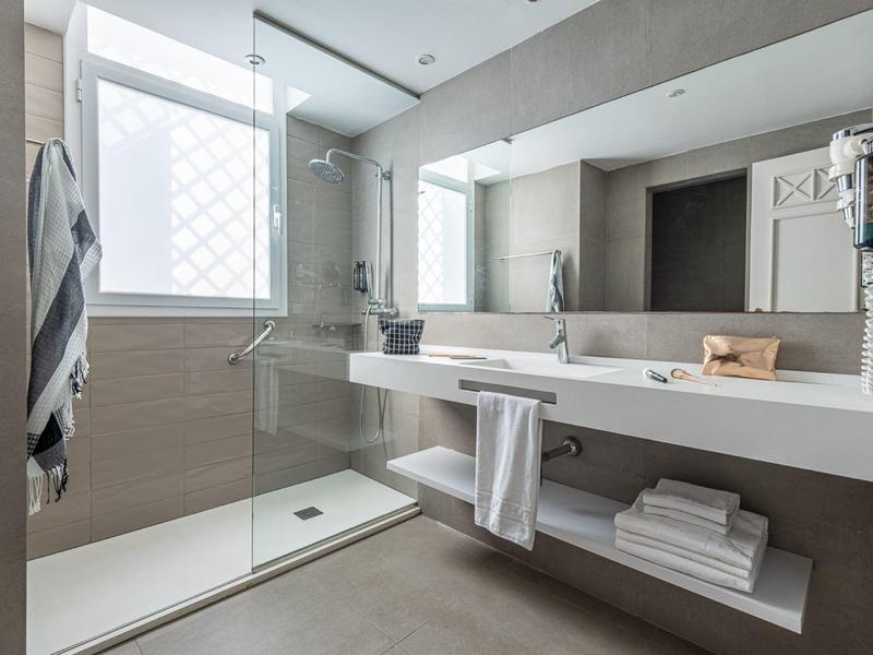 Modernes Badezimmer mit großer Glasdusche, weißem Waschbecken, großem Spiegel und grauen Fliesen.