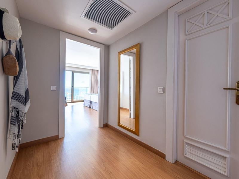 Heller Flur mit Holzboden, weißer Tür, großem Wandspiegel und aufgehängten Hüten und Taschen.