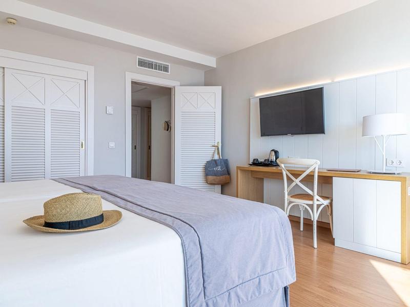 Helles Schlafzimmer mit weißer Bettdecke, Holzfußboden, Schreibtisch und Wandfernseher.