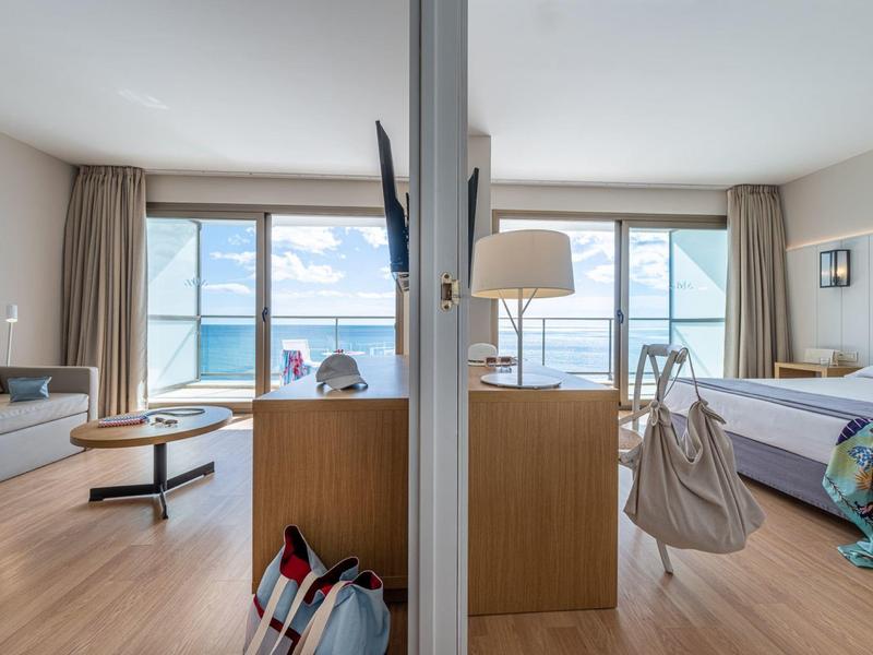 Modernes Hotelzimmer mit Meerblick, Holzmöbeln, Sofa, Bett, Teppich und großen Fenstern.