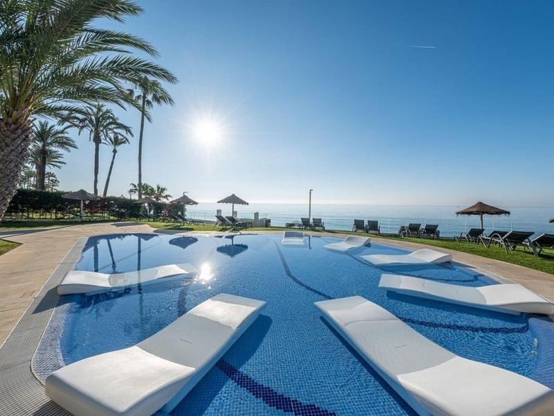 Schöner Pool mit eingebauten Liegen, Palmen und Meerblick bei Sonnenuntergang.