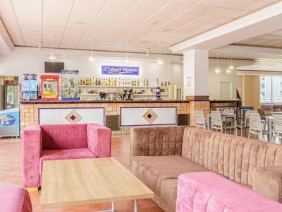 Heller Raum mit rosa und braunen Polstermöbeln, Holztischen und Bar mit Getränken im Hintergrund.