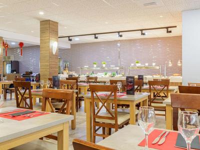 Hell eingerichtetes Restaurant mit Holzstühlen, gedeckten Tischen und Buffetbereich im Hintergrund.