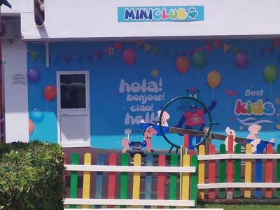 Bunte Fassade eines Kindergartens mit Spielplatz, Ballons und mehrfarbigem Lattenzaun.