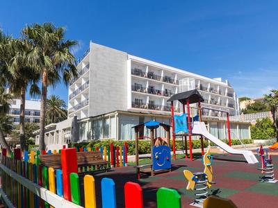 Bunter Kinderspielplatz mit Rutsche, Schaukeln vor modernem weißem Gebäude bei sonnigem Himmel.