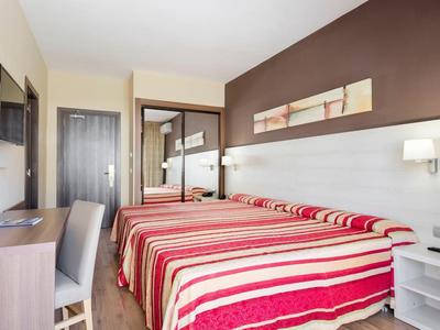 Hell eingerichtetes Hotelzimmer mit zwei Einzelbetten, gestreiften Bettdecken und brauner Akzentwand.