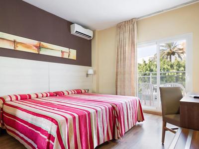 Hell eingerichtetes Schlafzimmer mit Doppelbett, gestreifter Bettdecke und Fenster mit Balkonblick.