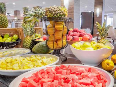 Bunter Obsttisch mit Wassermelone, Ananas, Orangen, Äpfeln und Mango in Schalen und Körben.