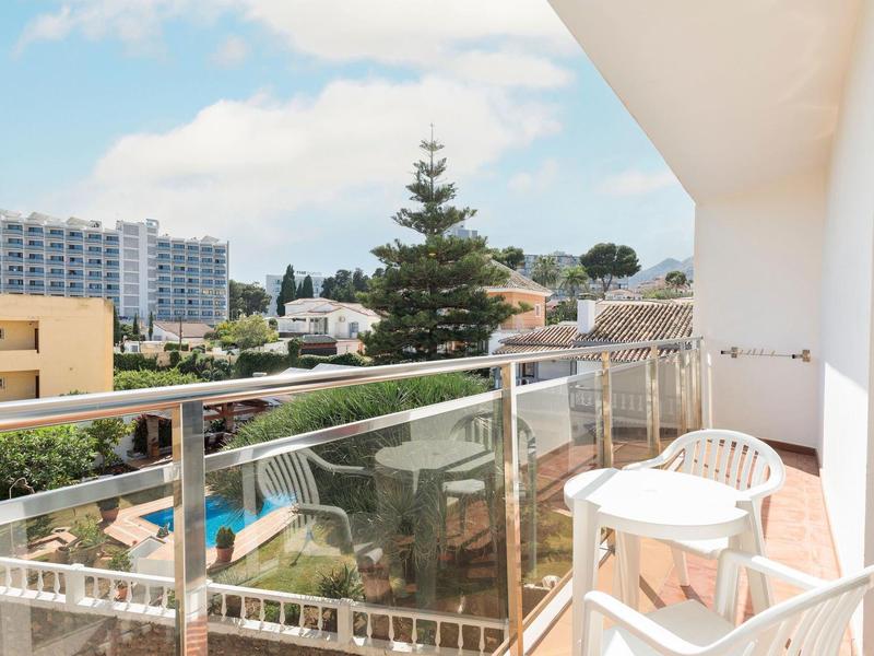 Balkon mit Glasgeländer, weißem Stuhl und Tisch, Blick auf Gebäude und Bäume bei Tageslicht.