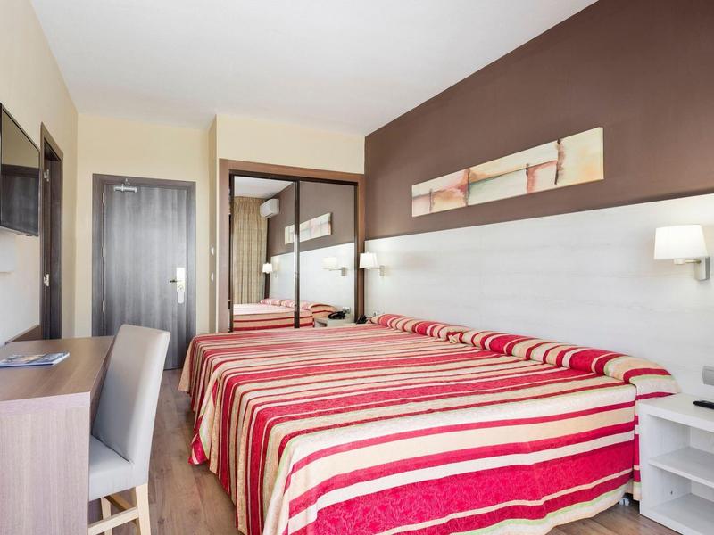 Hell eingerichtetes Hotelzimmer mit zwei Einzelbetten, gestreiften Bettdecken und brauner Akzentwand.